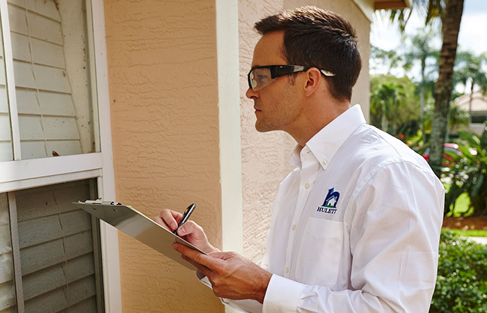 Pest control technician inspecting area around a window frame and making notes.