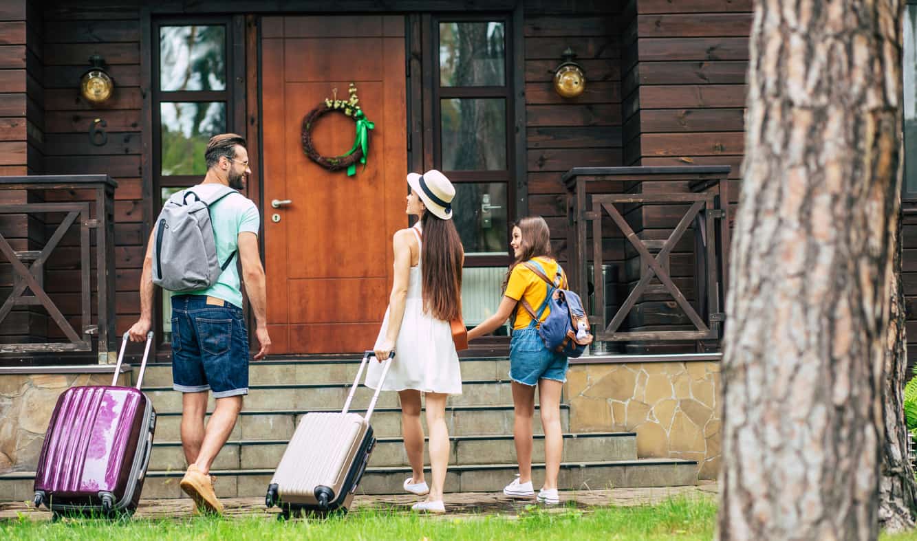 A family with suitcases approaches the front door of a home.