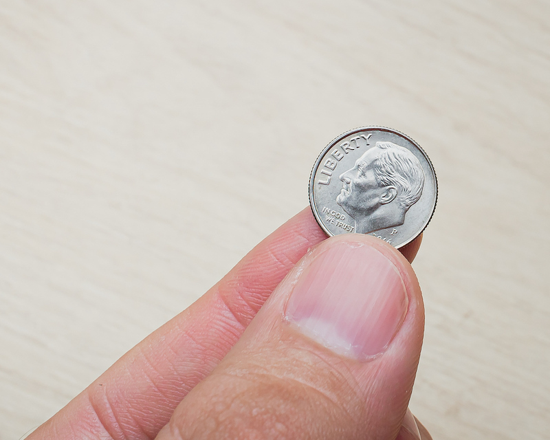 A dime is held between a person’s thumb and index finger.
