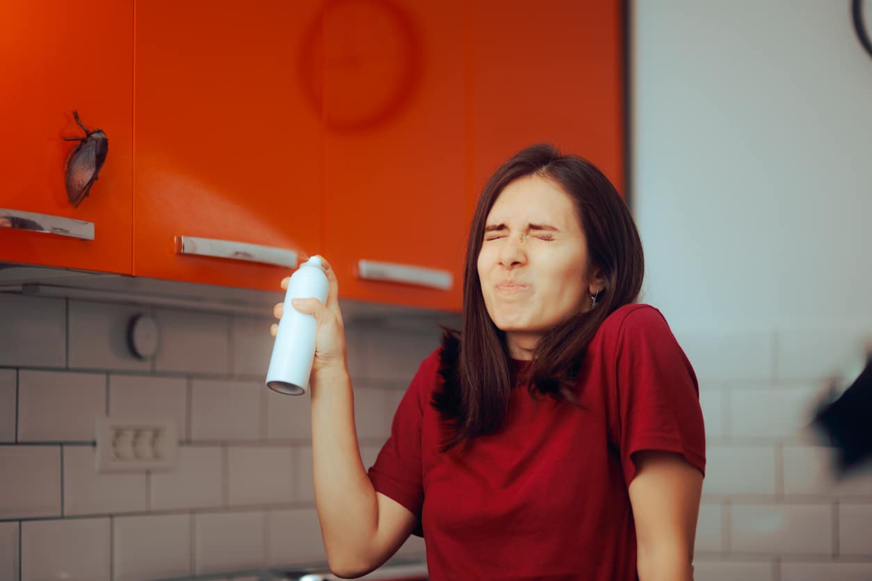 Flustered woman trying to use insecticide spray in the kitchen on a big cockroach