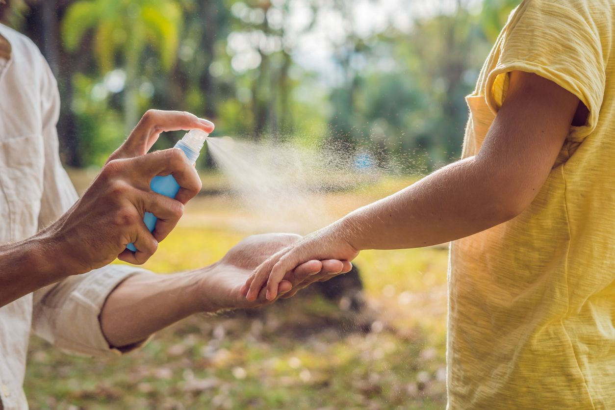 A mom spraying bug spray on her daughter