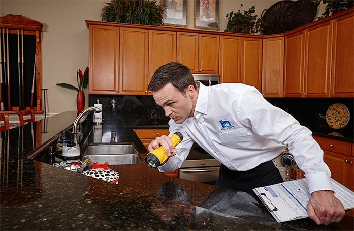 A Pest control technician inspects a kitchen for pests.